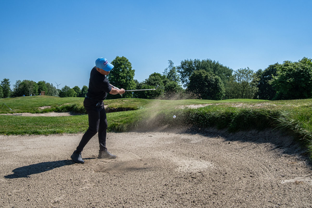 een golfspeler die zijn slag uit de bunker traint